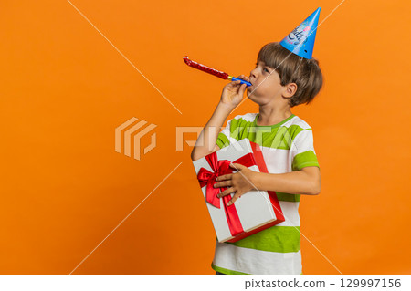 Happy excited lucky boy wearing birthday hat cone blow pipe celebrating party success win victory 129997156