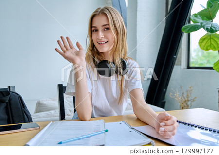 Webcam portrait female college student, sitting at home at the table with textbooks 129997172