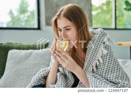 Young woman under blanket with cup with lemon, at home on sofa 129997197