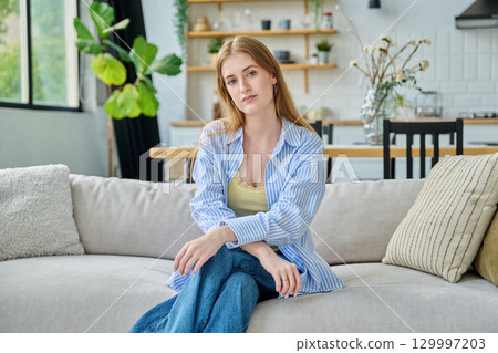 Portrait beautiful young woman at home looking at camera sitting on sofa 129997203
