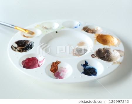 Colorful Artist Palette with Mixed Paints and Brush on Table 129997243