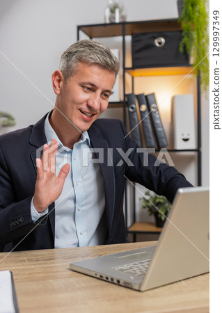 Confident Caucasian businessman in formal suit having online meeting with laptop at home office desk 129997349