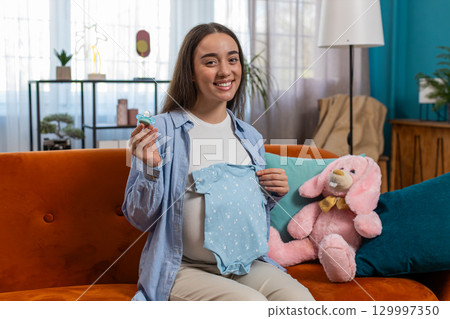 Pregnant woman looking at baby cloth and pacifier, preparing pregnancy, expecting baby, childbirth Pregnant woman looking at baby cloth and pacifier, preparing pregnancy, expecting baby, childbirth 129997350
