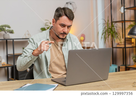 Confident Caucasian young male freelancer having video call via laptop sitting at home office table 129997356