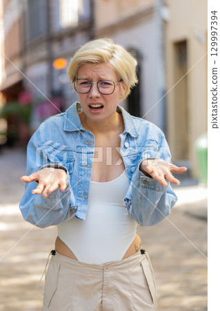 Doubtful sad frustrated young Caucasian woman shrugging shoulders dont know answer on city street Doubtful sad frustrated young Caucasian woman shrugging shoulders dont know answer on city street 129997394