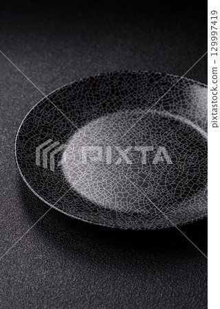 Empty round black plate for food, kitchen utensils on dining table. Empty plate 129997419