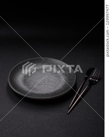 Empty round black plate for food, kitchen utensils on dining table. Empty plate Empty round black plate for food, kitchen utensils on dining table. Empty plate 129997477