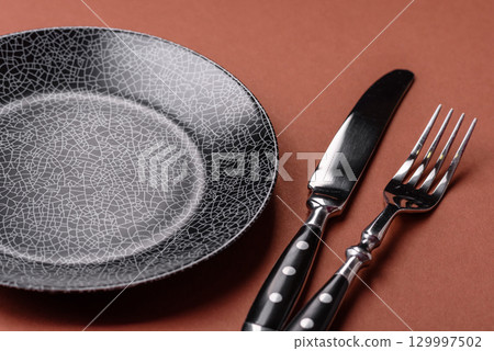 Empty round black plate for food, kitchen utensils on dining table. Empty plate 129997502