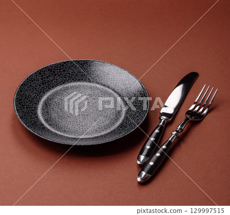 Empty round black plate for food, kitchen utensils on dining table. Empty plate 129997515