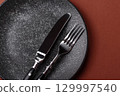 Empty round black plate for food, kitchen utensils on dining table. Empty plate 129997540