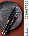 Empty round black plate for food, kitchen utensils on dining table. Empty plate 129997542