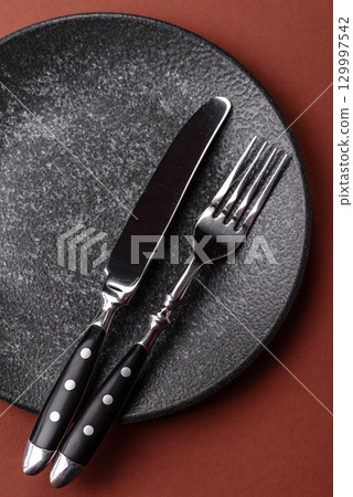 Empty round black plate for food, kitchen utensils on dining table. Empty plate 129997542
