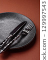 Empty round black plate for food, kitchen utensils on dining table. Empty plate 129997543