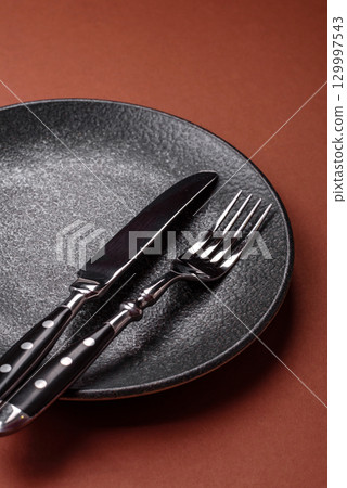 Empty round black plate for food, kitchen utensils on dining table. Empty plate 129997543