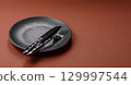Empty round black plate for food, kitchen utensils on dining table. Empty plate 129997544