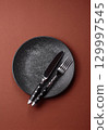 Empty round black plate for food, kitchen utensils on dining table. Empty plate 129997545