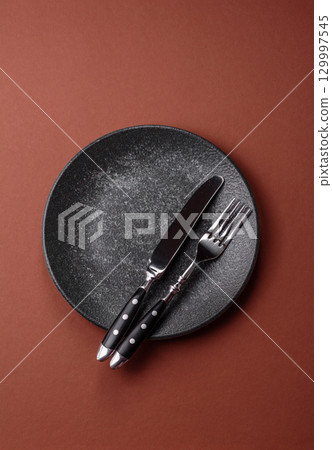 Empty round black plate for food, kitchen utensils on dining table. Empty plate 129997545