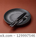 Empty round black plate for food, kitchen utensils on dining table. Empty plate 129997546