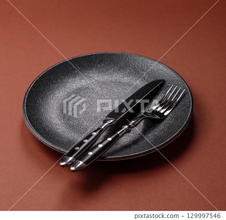 Empty round black plate for food, kitchen utensils on dining table. Empty plate 129997546