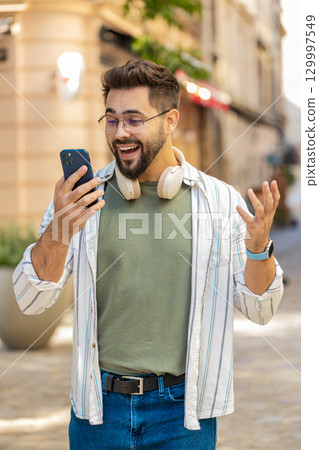 Happy young man using smartphone celebrating victory win good message news on city town street Happy young man using smartphone celebrating victory win good message news on city town street 129997549
