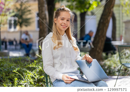 Happy young woman freelancer sitting in city street closes laptop screen finishing working online Happy young woman freelancer sitting in city street closes laptop screen finishing working online 129997571