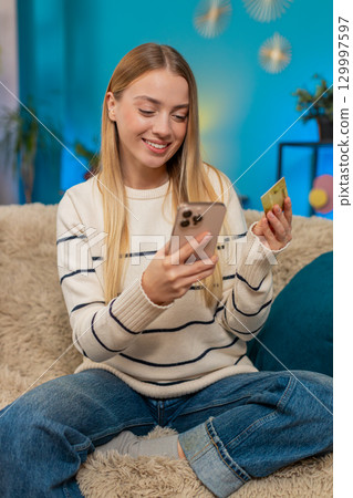 Caucasian woman paying purchase on sofa with mobile phone credit card smiling successful indoors 129997597
