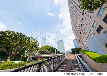 A view of an office district looking up at street trees, skyscrapers, and a pedestrian bridge 129998000