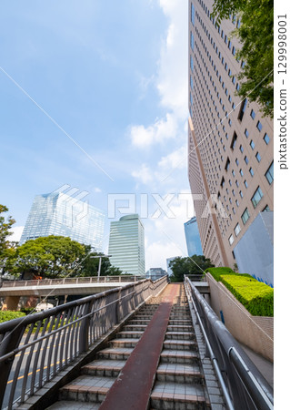 A view of an office district looking up at street trees, skyscrapers, and a pedestrian bridge 129998001