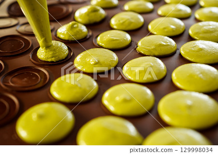 Close-up of young woman's hands making homemade pistachio macarons 129998034