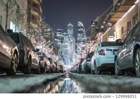 Night cityscape with glowing skyscrapers, reflections in wet pavement 129998051
