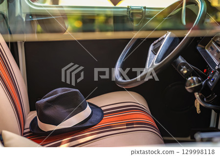 Salon with hat on seat. Interior of vintage car with striped seats and elegant fedora hat resting casually. Concept of retro lifestyle, stylish travel moments, adventure nostalgia Salon with hat on seat. Interior of vintage car with striped seats and elegant fedora hat resting casually. Concept of retro lifestyle, stylish travel moments, adventure nostalgia 129998118
