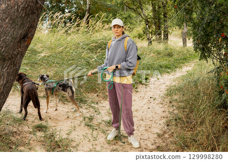 person walks two dogs on path in forest or park. Pet training with handler, professional dog walker. person walks two dogs on path in forest or park. Pet training with handler, professional dog walker. 129998280