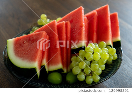 plate with watermelon and grapes stands on wooden table. 129998291