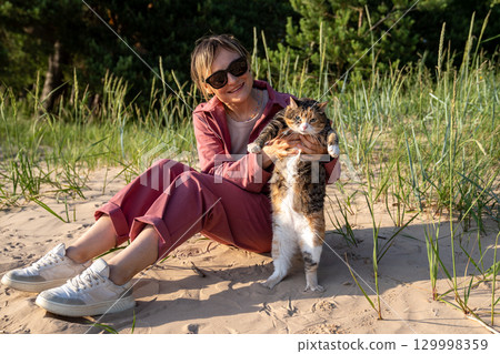 Smiling woman hold sulking cat with dramatic posture and frown, pet refuse to enjoy walk outdoors Smiling woman hold sulking cat with dramatic posture and frown, pet refuse to enjoy walk outdoors 129998359
