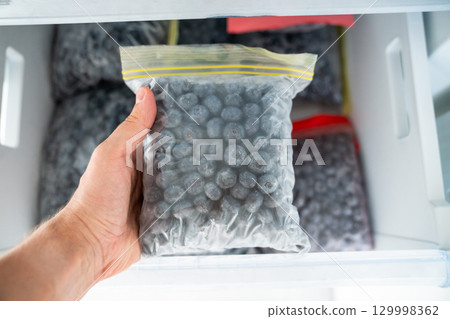 Man hands hold zip bag with blueberries, putting into freezer. Storing summer berry for future use Man hands hold zip bag with blueberries, putting into freezer. Storing summer berry for future use 129998362