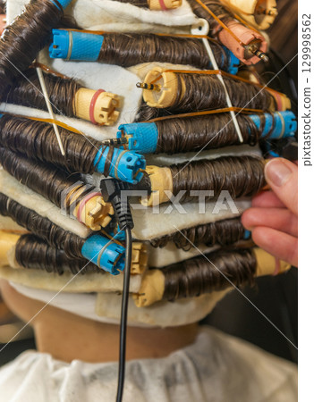 a young girl is getting her hair curled with curlers 129998562