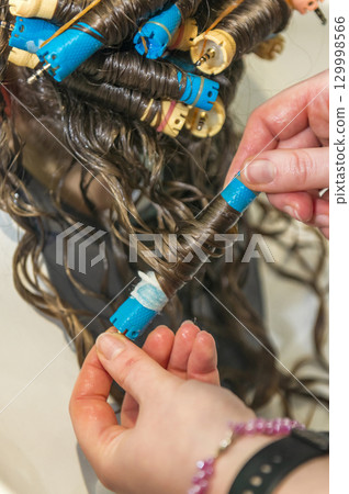 the hairdresser removes curlers from the client's hair. the hairdresser removes curlers from the client's hair. 129998566