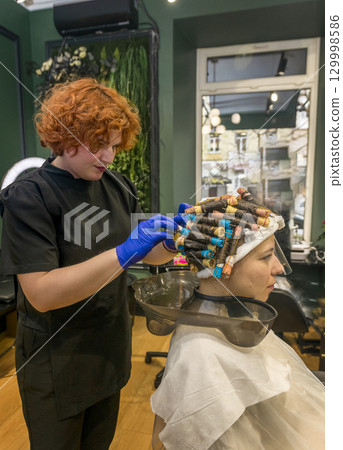a young girl is getting her hair curled with curlers 129998586