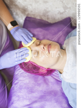 A cosmetologist wipes a woman client's face with sponges 129998591