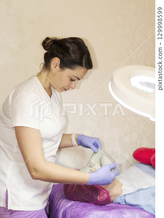 A female cosmetologist doctor makes a facial mask for a client 129998599