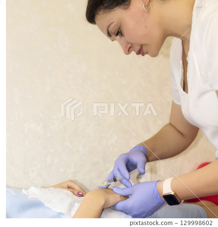 a cosmetologist gives a client an injection into the arm 129998602