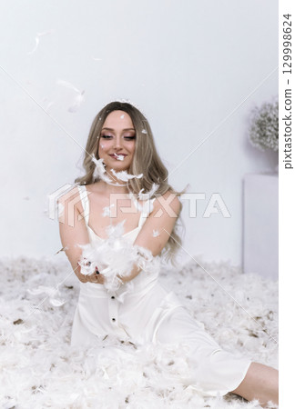 a very beautiful blonde sits in a white room in which feathers are flying a very beautiful blonde sits in a white room in which feathers are flying 129998624