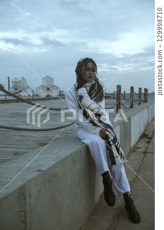 Beautiful young girl in a white tracksuit stands on the seashore in stormy weather Beautiful young girl in a white tracksuit stands on the seashore in stormy weather 129998710