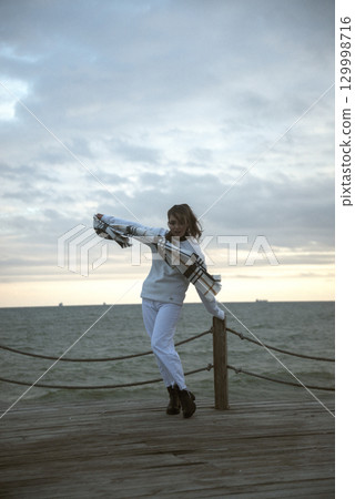 Beautiful young girl in a white tracksuit stands on the seashore in stormy weather Beautiful young girl in a white tracksuit stands on the seashore in stormy weather 129998716