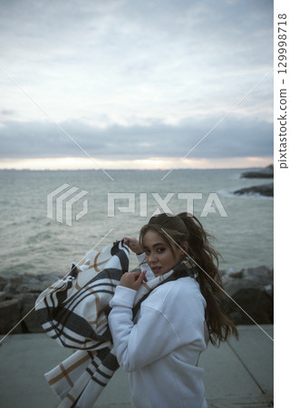 Beautiful young girl in a white tracksuit stands on the seashore in stormy weather Beautiful young girl in a white tracksuit stands on the seashore in stormy weather 129998718