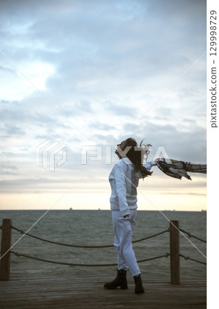 Beautiful young girl in a white tracksuit stands on the seashore in stormy weather Beautiful young girl in a white tracksuit stands on the seashore in stormy weather 129998729