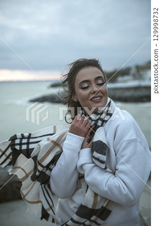 Beautiful young girl in a white tracksuit stands on the seashore in stormy weather 129998732