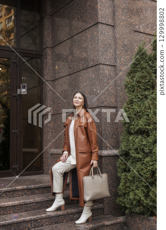 elegant woman over 40 exiting building with laptop bag elegant woman over 40 exiting building with laptop bag 129998802