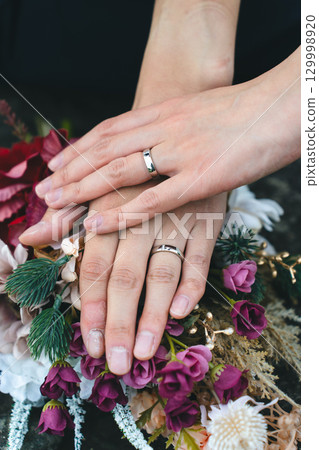 Hands clasped together over wedding rings and bouquet 129998920