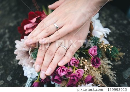 雙手緊握,捧著結婚戒指和花束 雙手緊握,捧著結婚戒指和花束 129998923